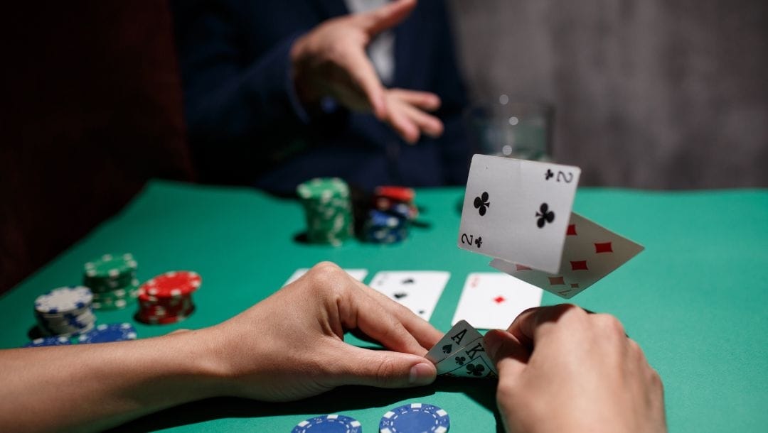 two players at a Texas Hold’em poker table, the closer person checks their hole cards and the player opposite throws their cards in