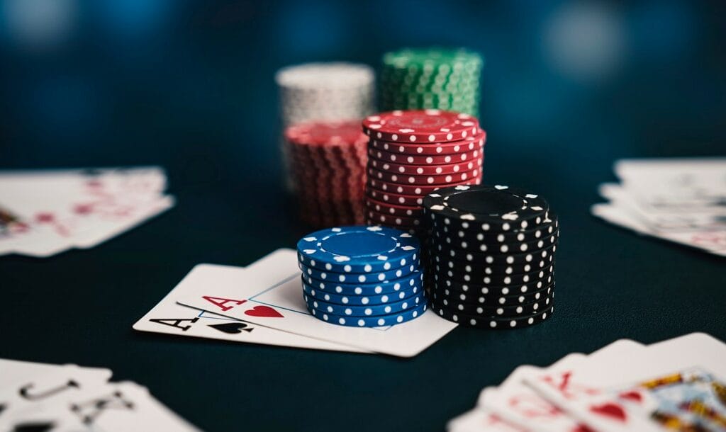 Stacks of poker chips on top of a pair of aces. Other poker hands are scattered around on the table.