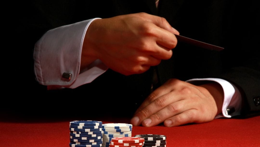 a man sitting at a red felt poker table, folding by throwing in his hole cards towards stacks of poker chips