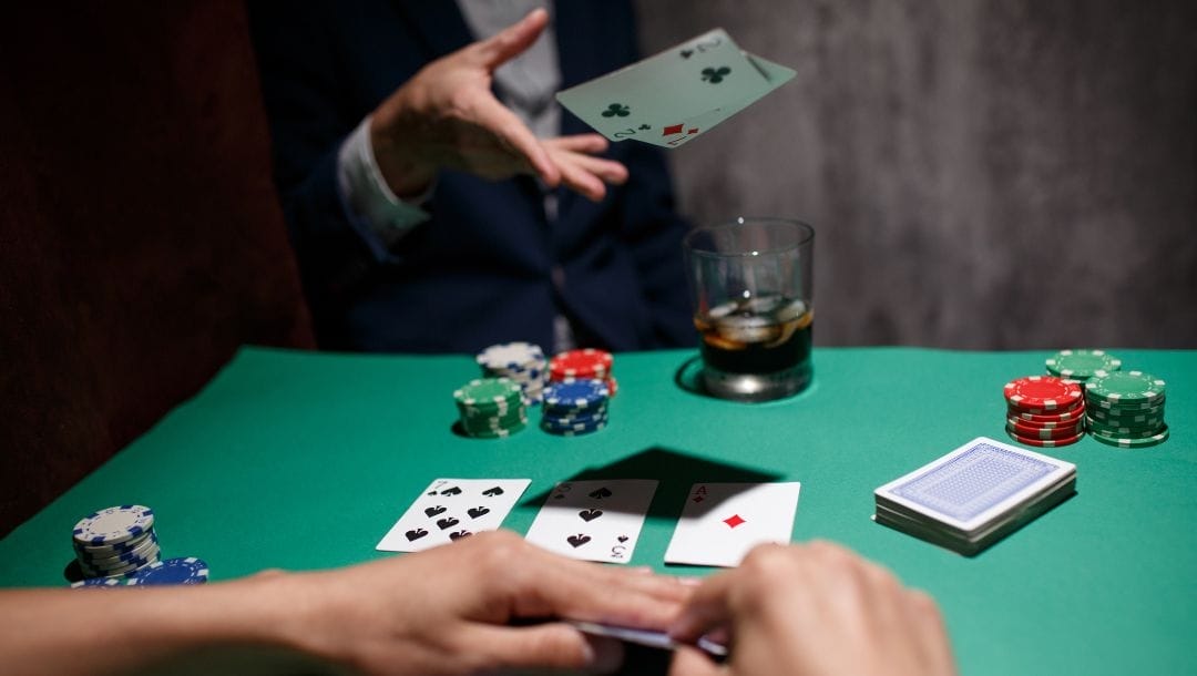 two people sitting opposite each other at a poker table, the man folds by throwing in his hole cards