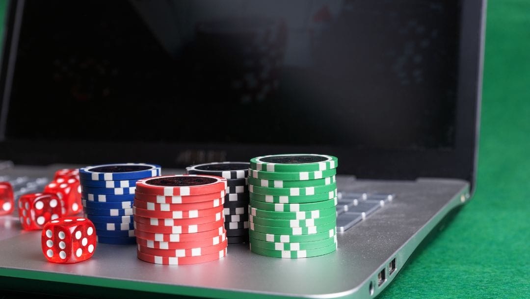 poker chips and red six sided dice on a laptop on a green felt poker table