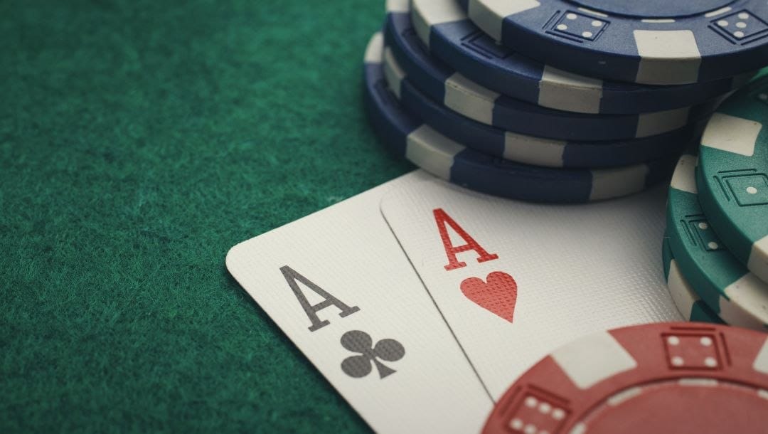 a pair of ace playing cards, a club and a heart, sticking out under stacks of poker chips on a green felt poker surface