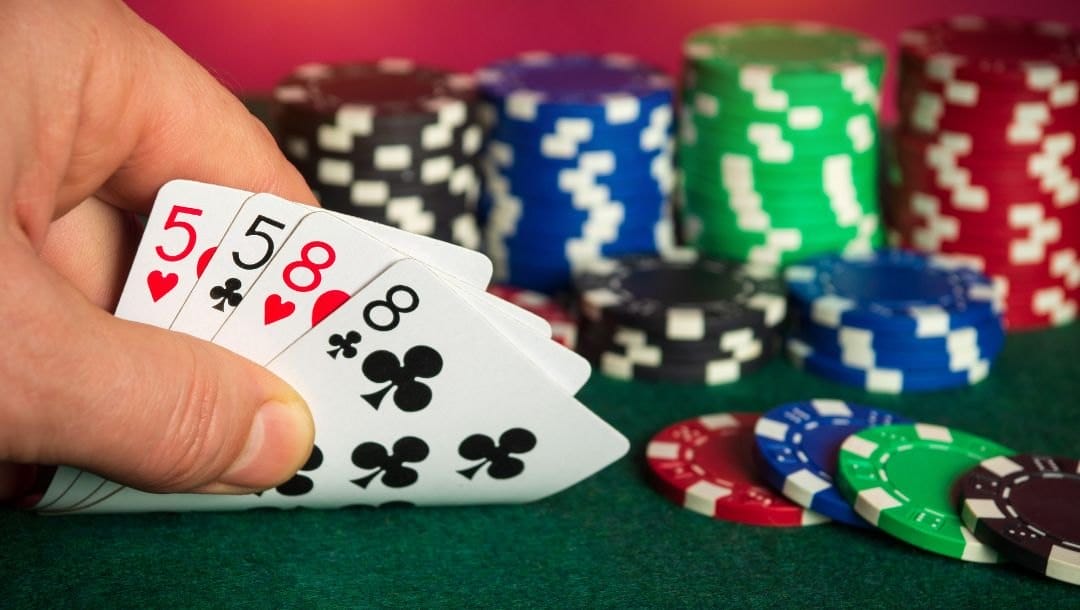 a close up of a person checking their hole cards, a pair of eights and a pair of fives, on a green felt poker surface with poker chips on it