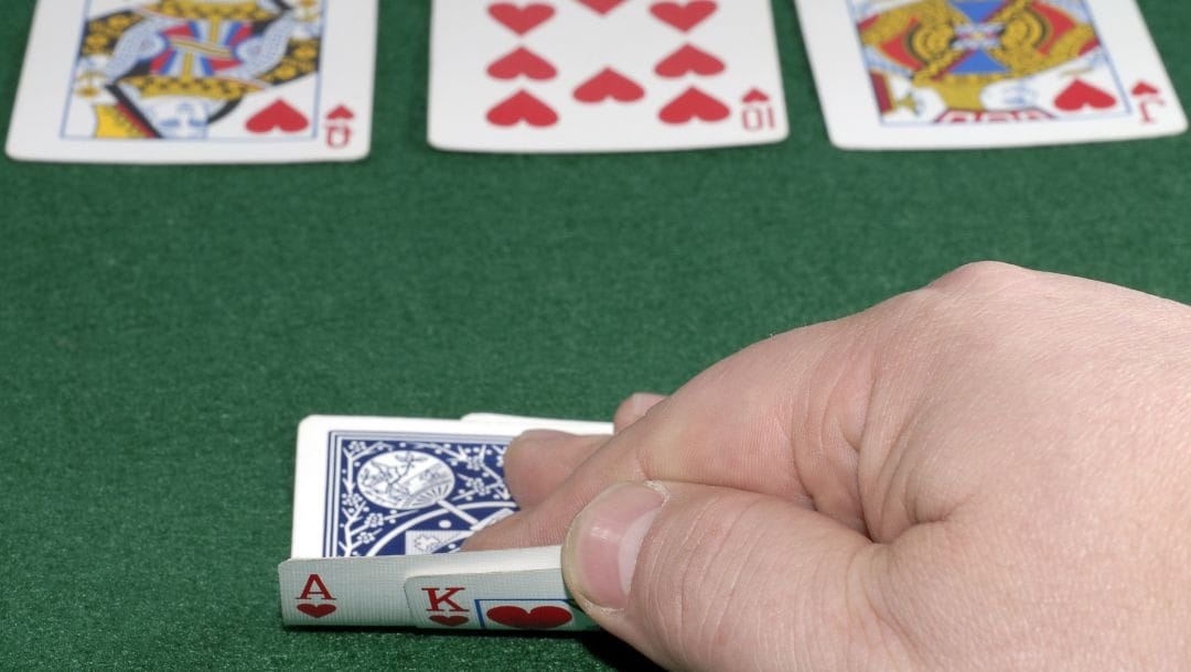 a man checking his hole cards, an ace and king of hearts, post flop during a game of poker where he has a royal flush