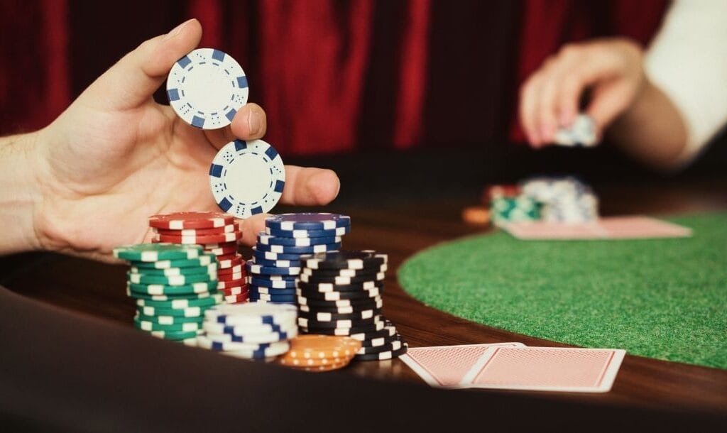 a close up of a person picking up poker chips from the stacks on a poker table with a player opposite them