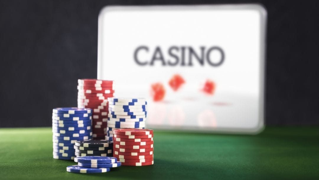 poker chips stacked on a green felt poker surface in front of a digital tablet displaying an online casino concept