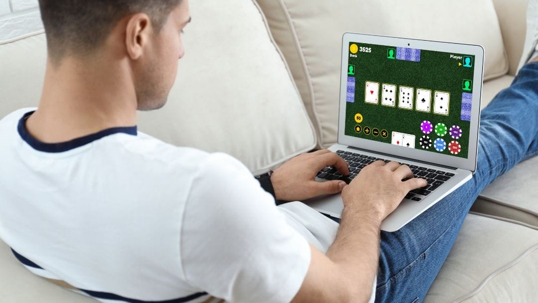 a man sitting with his legs up on a couch playing online poker on a laptop