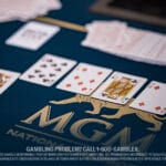A poker game on a blue table with "MGM" logo, showing a winning hand of spade and heart cards. A stack of cards is fanned out in the background.