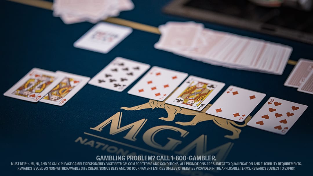 A poker game on a blue table with "MGM" logo, showing a winning hand of spade and heart cards. A stack of cards is fanned out in the background.