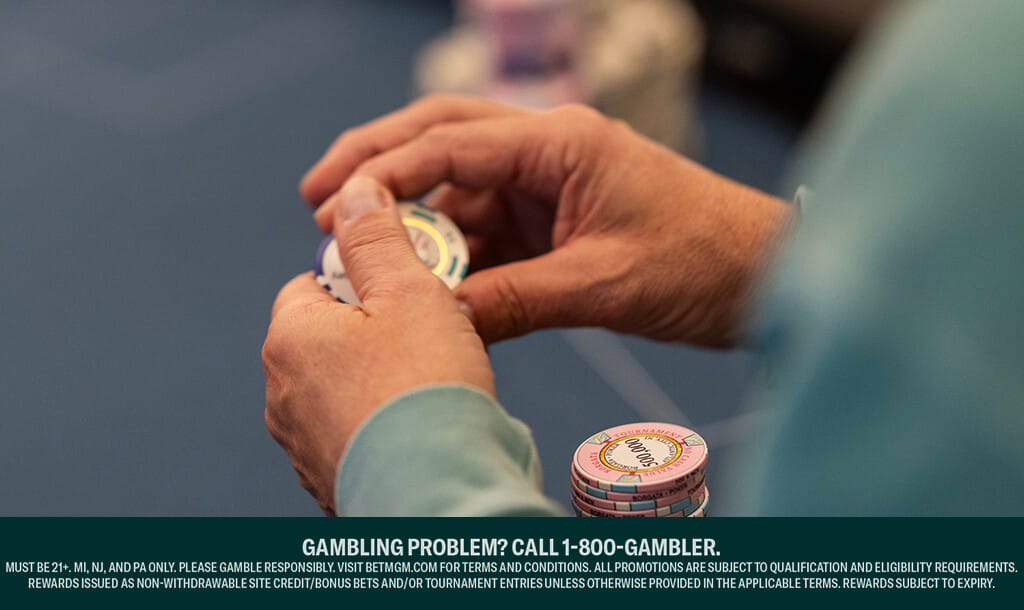 Close-up of a person holding poker chips at a casino table, with additional stacks of chips on the table.