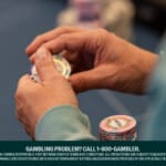 Close-up of a person holding poker chips at a casino table, with additional stacks of chips on the table.