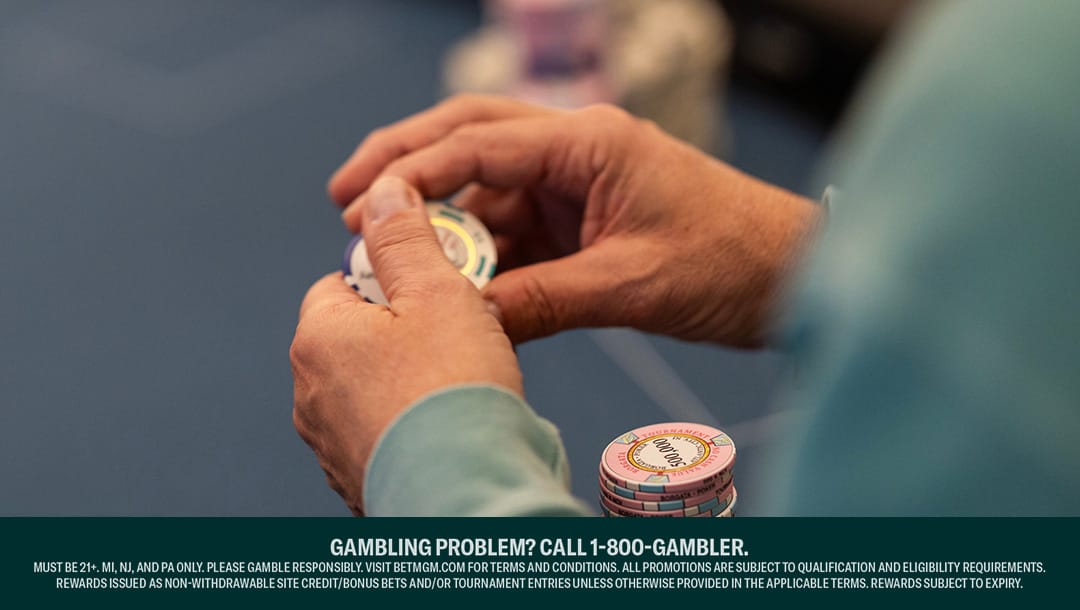 Close-up of a person holding poker chips at a casino table, with additional stacks of chips on the table.