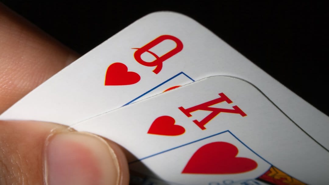 An extreme close-up of a poker player’s hole cards. They have a queen and king of hearts.