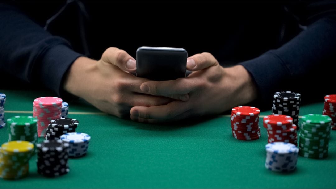 A person at a poker table holding their phone.