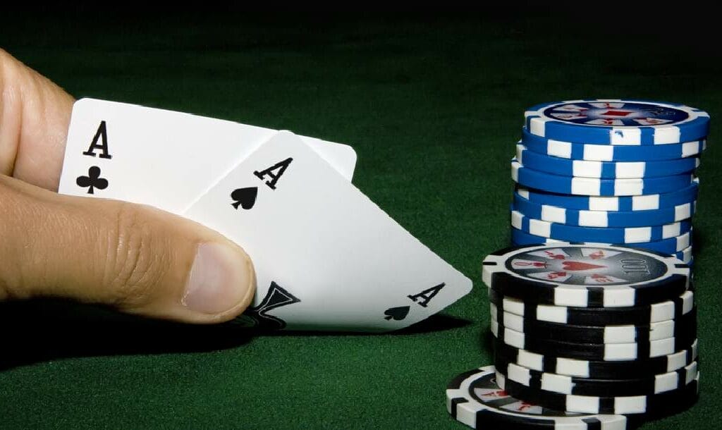 A player looks at an ace-pair next to chips on a poker table.