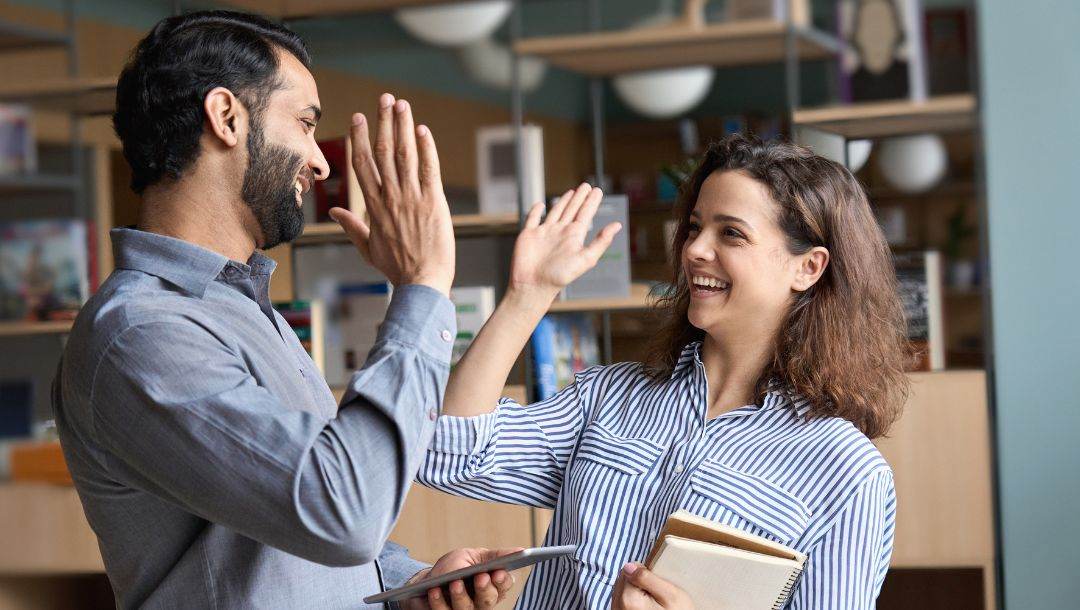 Two happy friends give each other a high five while laughing.