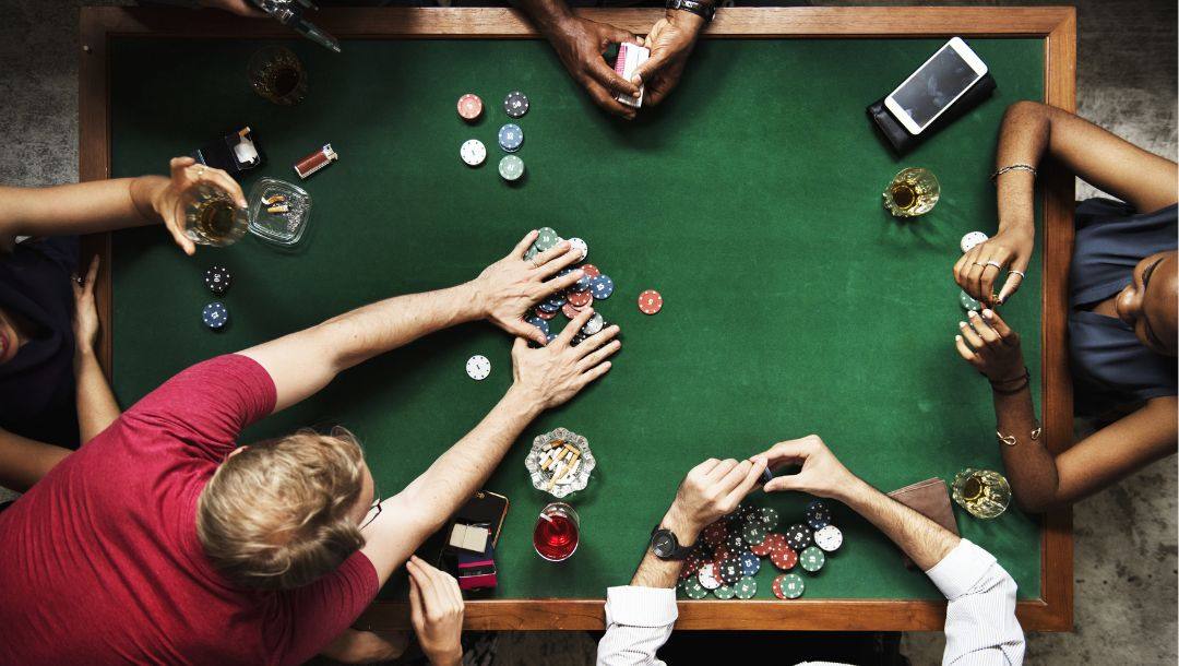 A group of individuals seated around a green poker table, engaged in a game of poker.