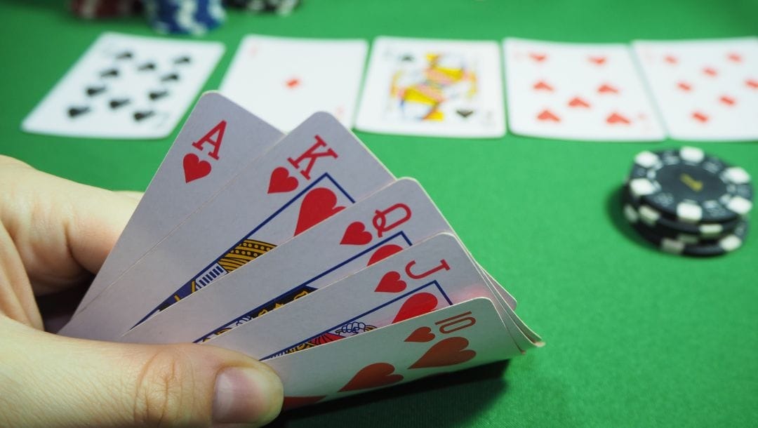 An individual seated at a poker table, revealing their cards: King, Queen, Jack, and 10 of hearts.