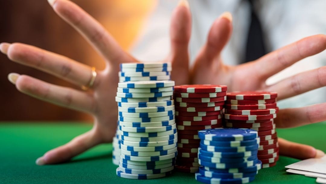 a person’s hands with their fingers spread out pushing stacks of poker chips forward with the palms on a green felt poker table