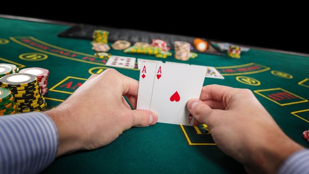 Hands of a man holding playing cards at a poker table. Poker chips are scattered on the table's surface