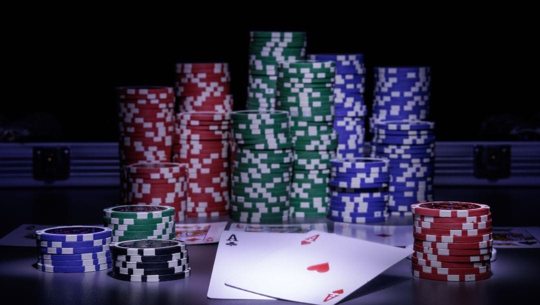 15 stacks of poker chips placed around poker playing cards in dark ambient lighting with a spotlight illuminating the pair of Aces.