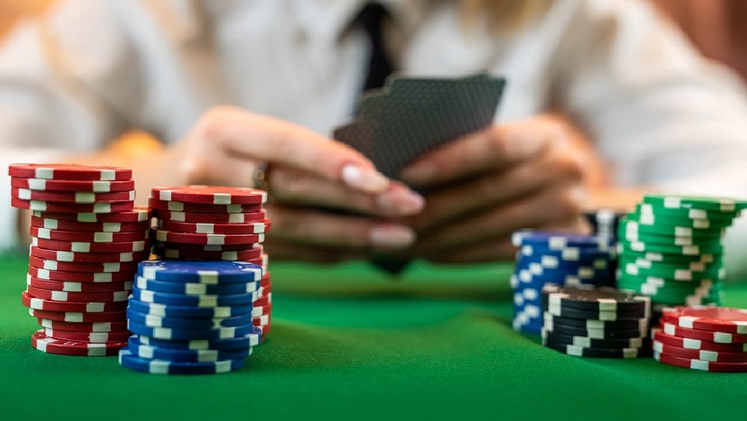 A woman with some cards in her hand blurry in the background with in focus poker chips in the foreground