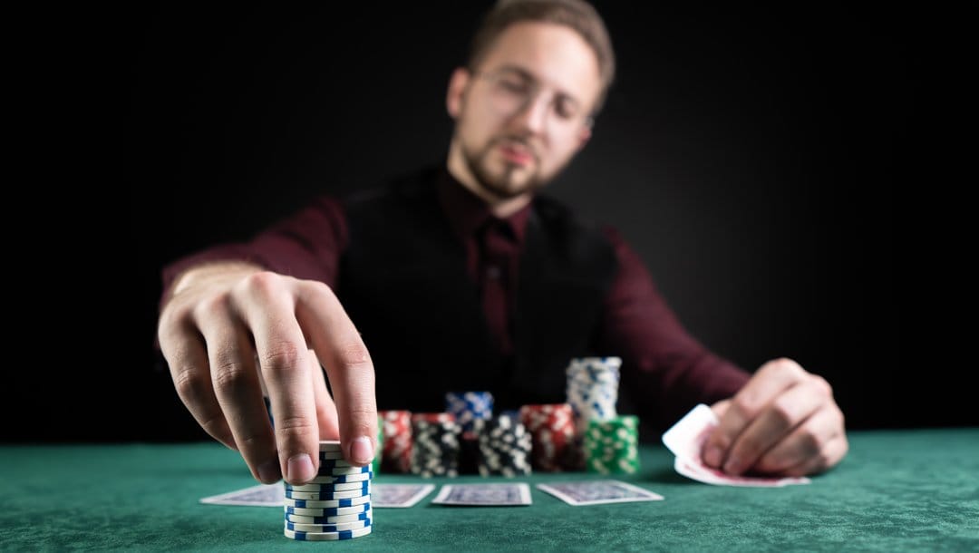 A poker player placing down a stack of chips for his next poker bet. He is bending his hole cards so he can see them.
