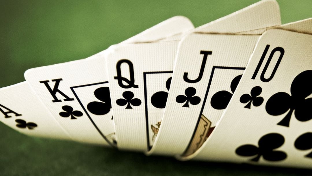 a royal flush of clubs playing cards being lifted up on a green felt poker table