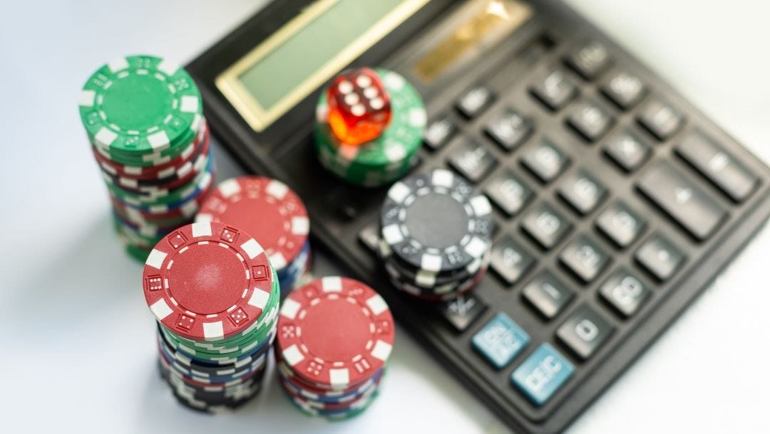 a top view of a calculator with poker chips and a red six-sided dice on top and next to it