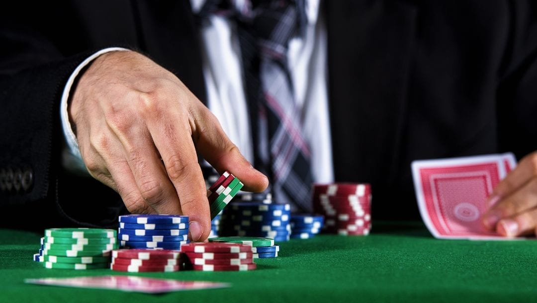 a man picking up from stacks of poker chips from a green felt poker table