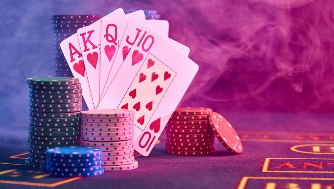 A photograph showing a Royal Flush in the hearts suit, next to stacks of poker chips, in purple ambient lighting.