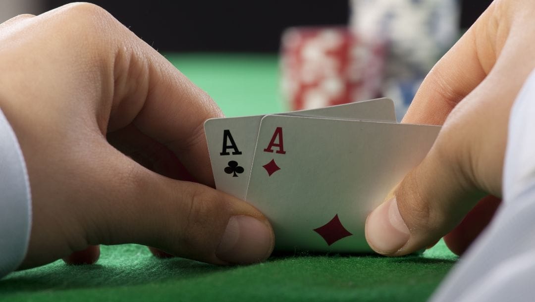 a person checks their hole cards, a pocket pair of aces, on a green felt poker table with poker chips in the blurred background