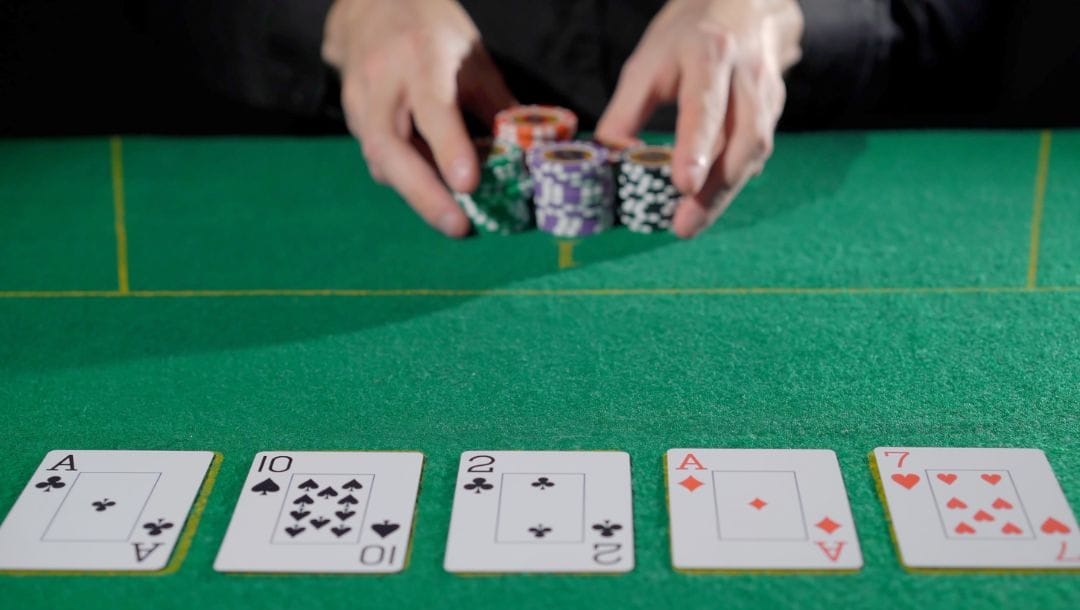 a person pushing their poker chips forward on a green felt poker table with playing cards face up on it