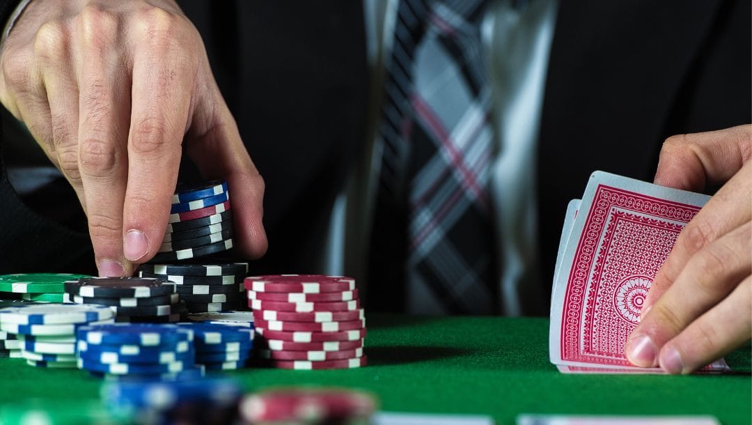 a man checking his hole cards on a green felt poker table while picking up from a stack of poker chips with his other hand