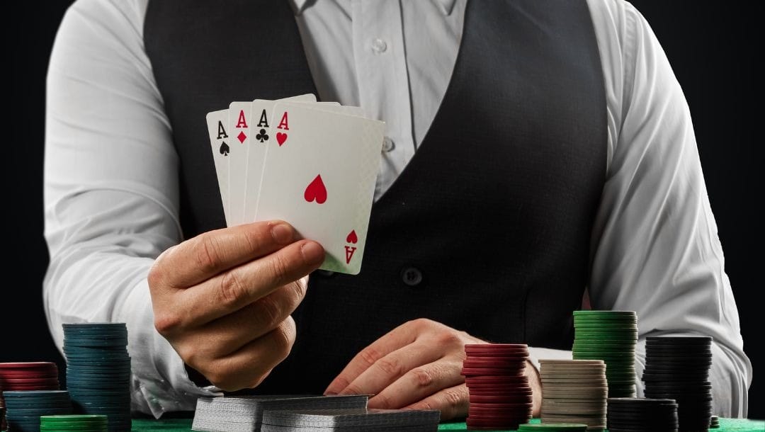 a man in a smart shirt and suit vest is holding up four of a kind ace playing cards above a poker table with other playing cards and stacks of poker chips on it