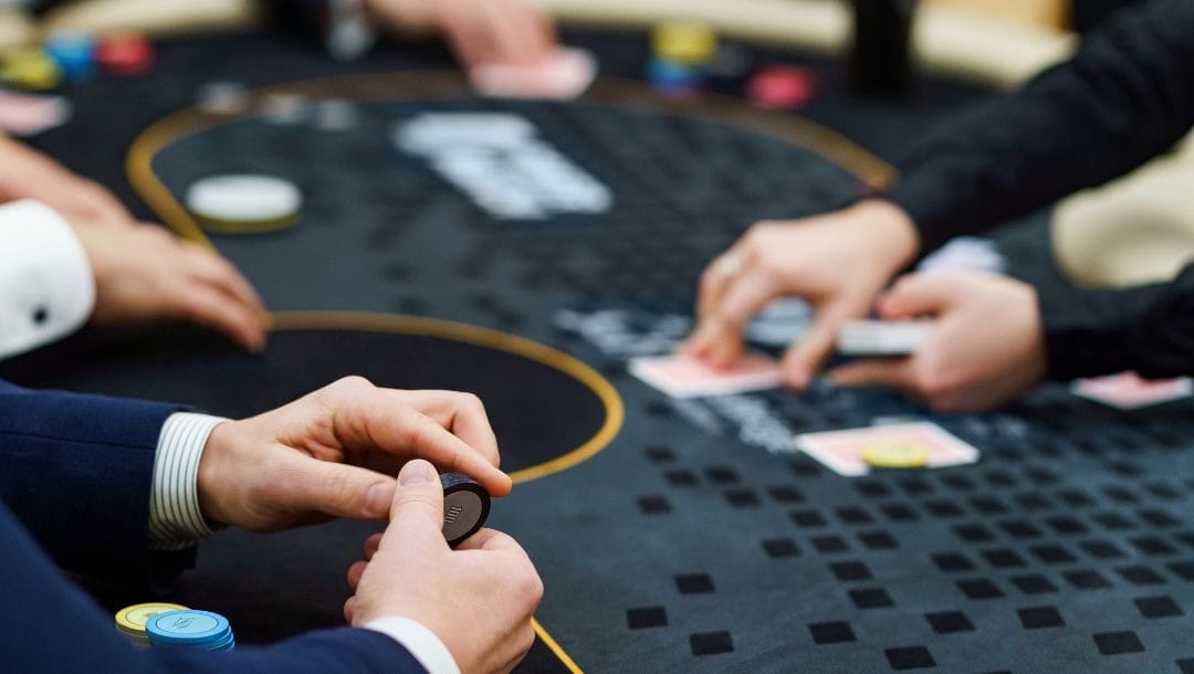 a man is holding black poker chips in his hand at a poker table during a poker game with other players in a casino