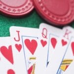 a royal flush of hearts between poker chips and dice on a green felt poker table