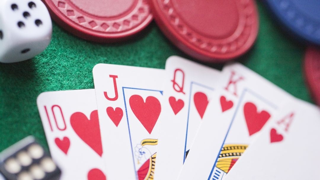 a royal flush of hearts between poker chips and dice on a green felt poker table