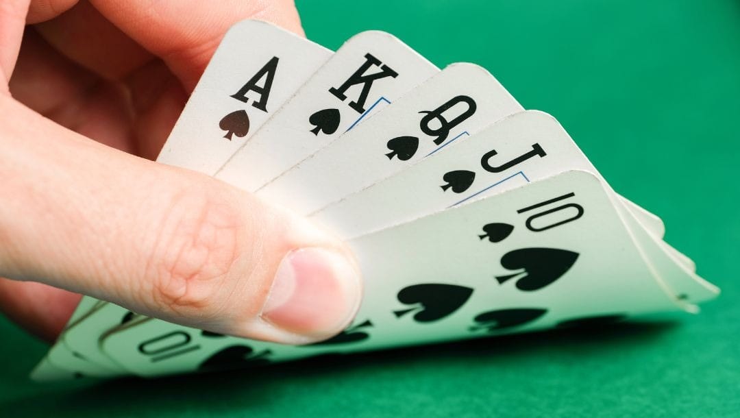 fingers lifting up royal flush of spades on a green felt poker table