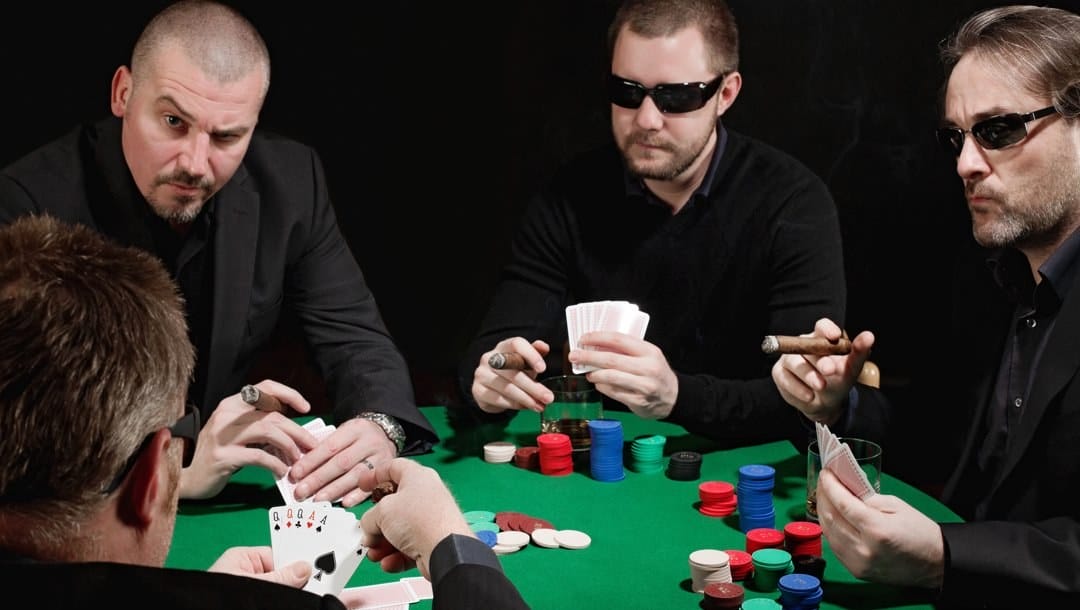 Three poker players in dark suits looking at another poker player during a game.