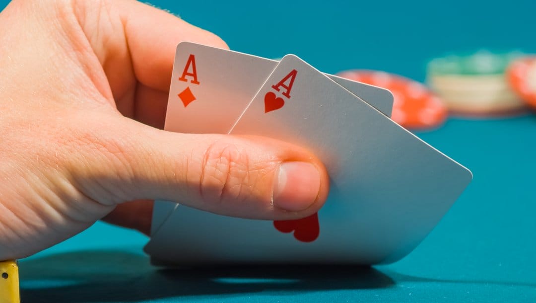 A poker player checks their hole cards. They have two aces.