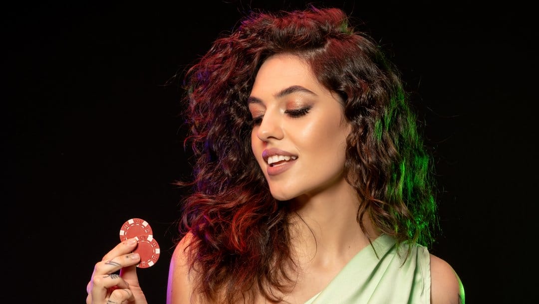A woman in a green dress looking at two casino chips in her hand.