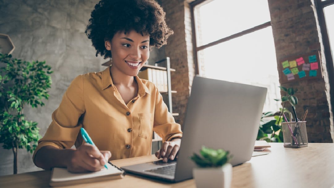 A young woman takes notes while on her laptop