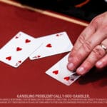 A hand is placing playing cards, including a five of hearts, on a red table, suggesting a poker game.