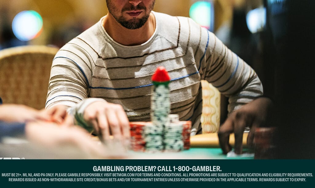 A focused poker player in a striped sweater sitting at a casino table, stacking a large pile of poker chips with a single red chip on top. Other players' hands are visible in the foreground.