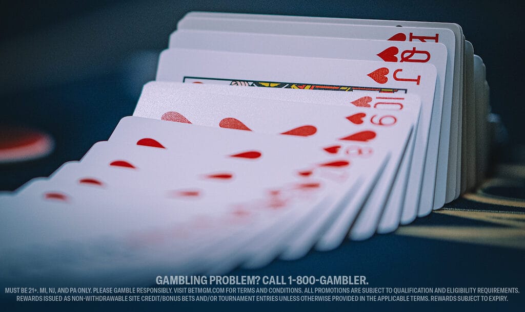 A fanned deck of playing cards, featuring hearts, spreads across a dark poker table. The focus is on a Jack of Hearts.