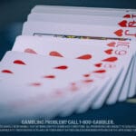 A fanned deck of playing cards, featuring hearts, spreads across a dark poker table. The focus is on a Jack of Hearts.