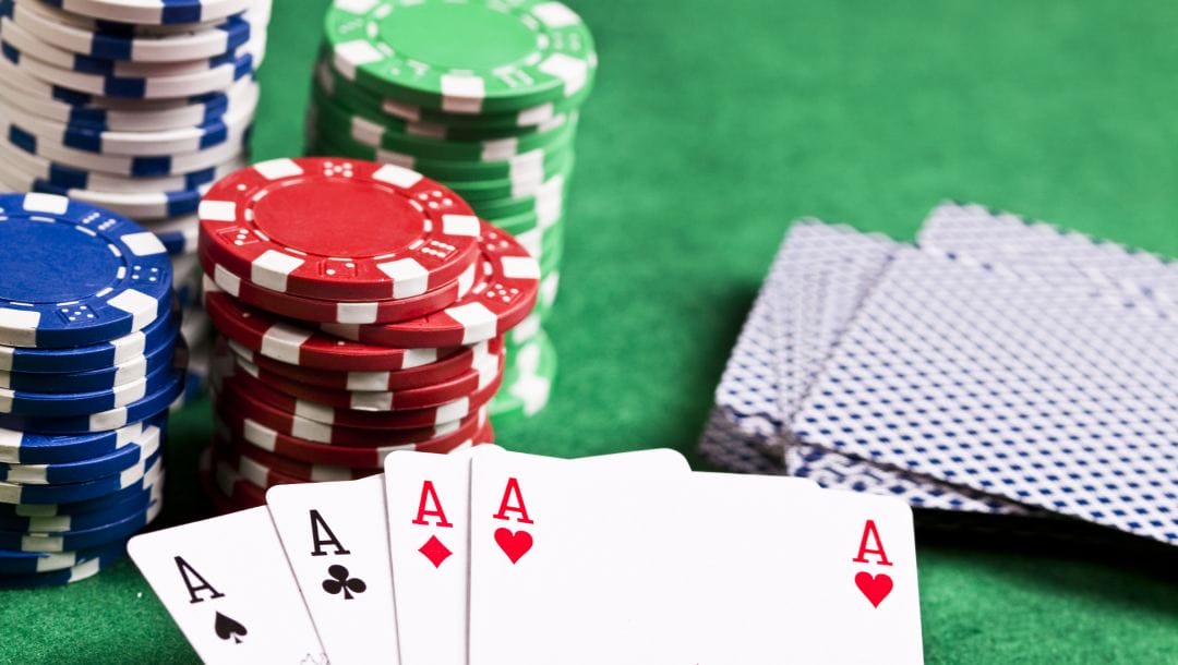 Stacks of poker chips and a spread hand of four aces on a green felt surface.