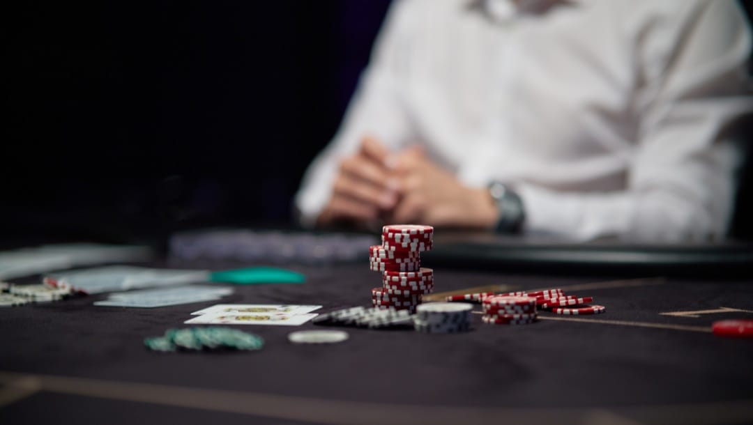 Poker chips on a black table with a man in the background.