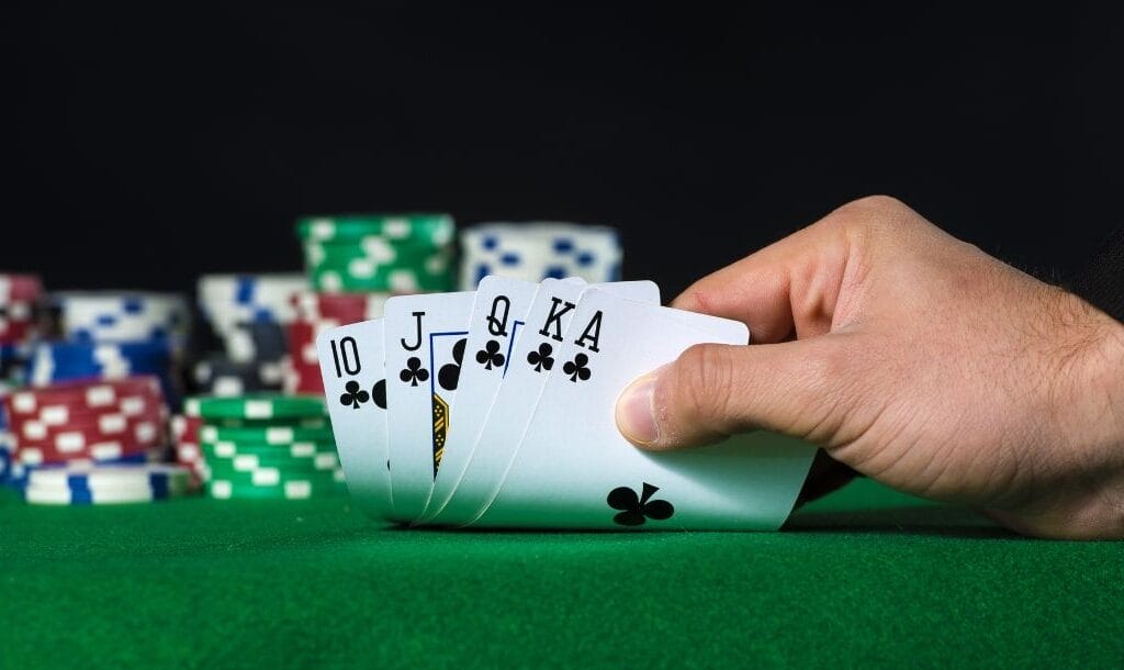 A hand holding Royal Flush in poker and poker chips chips arranged on a poker table.